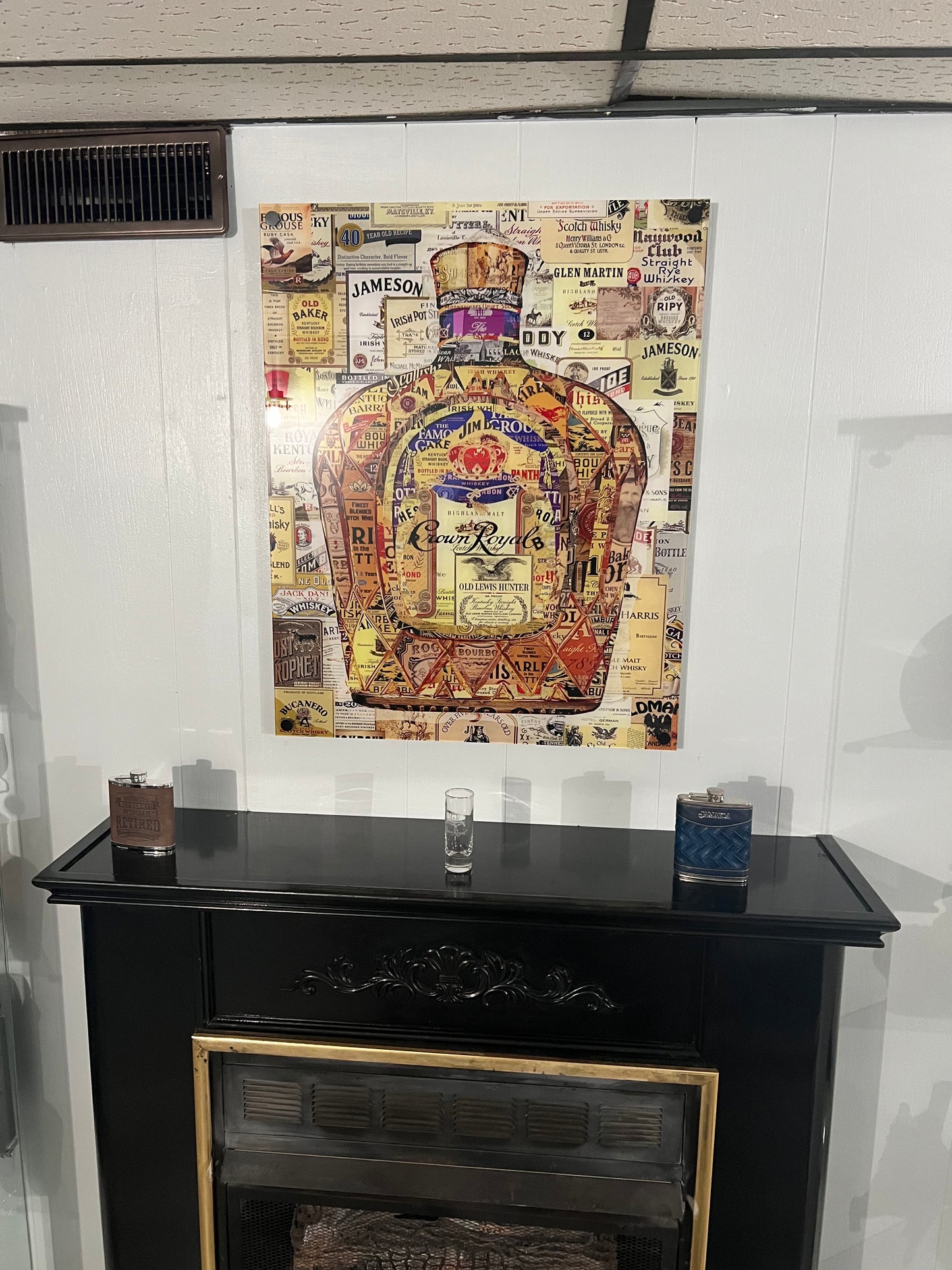 Decorative wall art with vintage-style bottle design on a white wall above a black cabinet.
