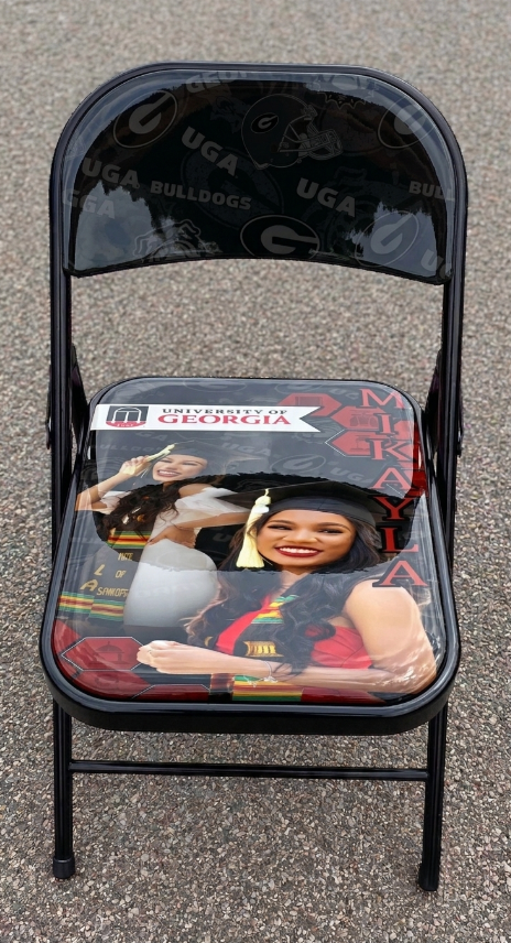 A black folding chair with a clear vinyl seat cushion featuring a printed graphic of a woman in a graduation cap and the text 'UNIVERSITY OF GEORGIA' and 'Majors & Minor'.